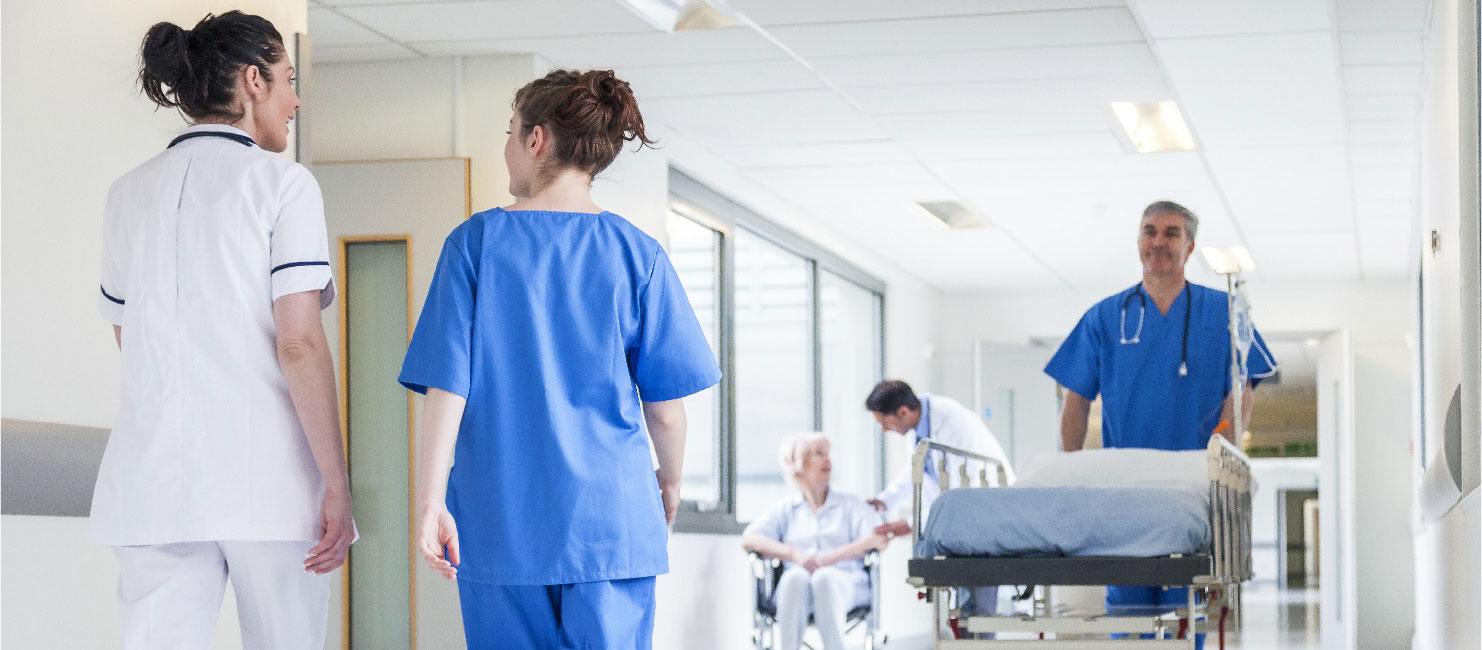An intern and a nurse walk through a busy hospital hallway